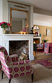 Pink upholstered armchair at fireplace with lit candles in Sussex home England UK