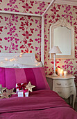 Bright pink cover on four poster bed with floral paper in South London home England UK