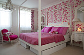 Storage below four poster bed with floral paper and lit candles in South London home England UK