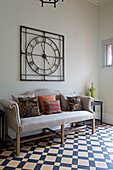 Large metal clock above upholstered sofa with cushions in tiled entrance hall of Worcestershire home England UK