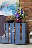 Glassware and crockery in blue sideboard with exposed brick wall in Sussex home England UK