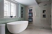 Freistehende Badewanne unter dem Fenster mit Jalousien und wandmontiertem Handtuchhalter in einem Haus in Sussex, England UK