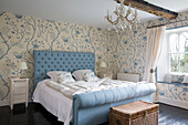 Glass chandelier hanging above light blue double bed with white duvet in Gloucestershire farmhouse England UK