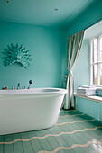 Freestanding bath at window with wall mounted mask in turquoise bathroom of Gloucestershire farmhouse England UK