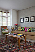 Armchair and sofa with vintage coffee table and bright scatter cushions in London living room England UK