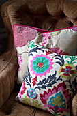 Floral cushions on buttoned brown armchair in Sussex home England UK
