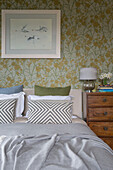 Flying geese framed on floral wallpaper above double bed with wooden chest of drawers in Kelso home Scotland UK