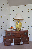 Lamp and feather on brown leather suitcases with bee patterned wallpaper in Kelso home Scotland UK