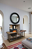Black circular mirror frame above open hearth with wood burning stove in Gloucestershire home England UK