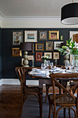 Schwarze Bilderwand mit Esstisch und Stühlen aus Holz in einem Haus in Gloucestershire England UK