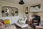 Recessed mirror and sideboard in living room with lit fire in Gloucestershire home England UK