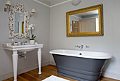 Gilt framed mirror above grey freestanding bath in Gloucestershire home England UK