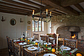 Candlelit dining table with lit fire at Christmas in timber-framed Hampshire farmhouse England UK