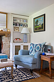 Framed artwork above light blue armchair with wooden side table in Gloucestershire cottage UK