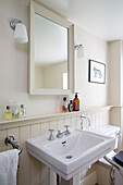 Spiegel über dem Waschbecken mit Toilettenartikeln in einem Cottage in Gloucestershire UK