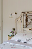 Antique headboard with floral pillow and wall sconce in London townhouse UK