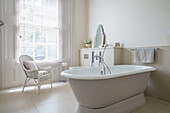 Wicker chair at window with freestanding bath in London townhouse UK