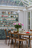 Wooden dining table and chairs with display cabinet in conservatory extension of London townhouse UK