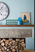 Clock above stone lintel with firewood in light blue Yorkshire kitchen England UK