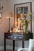 Cream lamp and cut flowers with lit candles on wooden side table in Cheshire living room UK