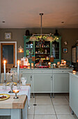 Schrank mit grüner Glasfront und brennenden Kerzen in einer Küche in Cheshire, UK