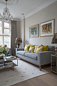 Yellow cushions on grey sofa below framed artwork in London townhouse UK