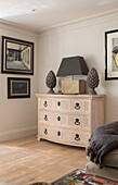 Grey lamp and artwork with wooden chest of drawers in West Sussex home