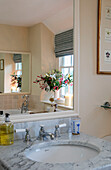 Lilien und Beeren spiegeln sich im Badezimmerspiegel mit Marmorwaschbecken in einem Bauernhaus in Dorset UK
