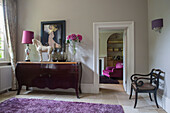 Pink flowers and lamp on vintage sideboard with view through doorway to armchair in detached Sussex country house UK