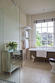 Mirrored chest of drawers with freestanding bath at window in detached Sussex country house UK
