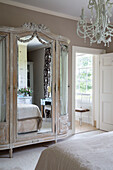 Antique mirrored wardrobe and chandelier with view to ensuite from bedroom in detached Sussex country house UK
