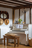 Holzhocker am weißen Klavier mit Sonnenhüten und Notenblättern in einem umgebauten Bauernhaus in Kent UK