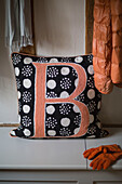 Orange jacket and gloves with letter B on black spotted cushion in Oast house conversion Kent UK