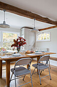 Silver folding chairs at wooden dining table with leaf arrangement in Oast house conversion Kent UK