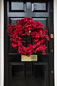 Kranz aus roten Beeren an schwarzer Haustür eines Londoner Stadthauses UK