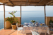Tisch und Stühle auf der sonnigen Balkonterrasse einer italienischen Villa an der Amalfiküste