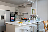 Upright fridge and spray tap with stools at breakfast bar in kitchen of London home UK