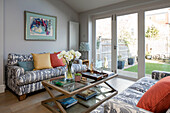 Grey sofas with wooden glass topped coffee table and view to garden in London home UK