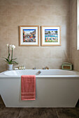 Orchid and radio on bathtub below framed artwork in London home UK