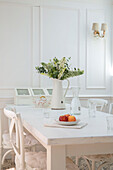 Cut flowers and apples on white dining table with chairs in Edwardian house Surrey UK