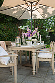 Cream table and chairs below parasol on terrace in Edwardian garden Surrey UK