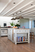 Metal pendant shades above island unit with recipe books in West Sussex farmhouse kitchen UK