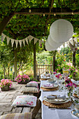 Papierschirme hängen an einer Pergola über einem Esstisch mit Sitzkissen und Wimpeln im Garten von Alford in Surrey, Großbritannien