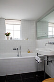 Geflieste Badewanne und Waschbecken unter dem Fenster in einem umgebauten Schulhaus in Südlondon UK