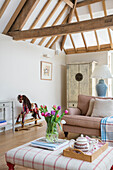 Tulpen und Teeservice mit Schaukelpferd in einem mit Balken versehenen Wohnzimmer in einer umgebauten Scheune in Gloucestershire UK
