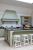 Weiße Hocker an der Frühstücksbar in einer Küche mit hellgrünem Dunstabzug in einer umgebauten Scheune in Gloucestershire UK
