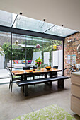 Tisch und Sitzbänke mit freiliegender Ziegelwand in einem Glasanbau eines viktorianischen Londoner Stadthauses UK