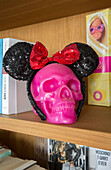 PInk skull with Mickey Mouse ears on wooden bookshelf in Victorian London townhouse UK