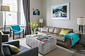 Framed artwork above sofa with turquoise blanket and chair in bay window of London home UK