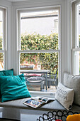 Turquoise cushions on window seat with view of backyard in London home UK